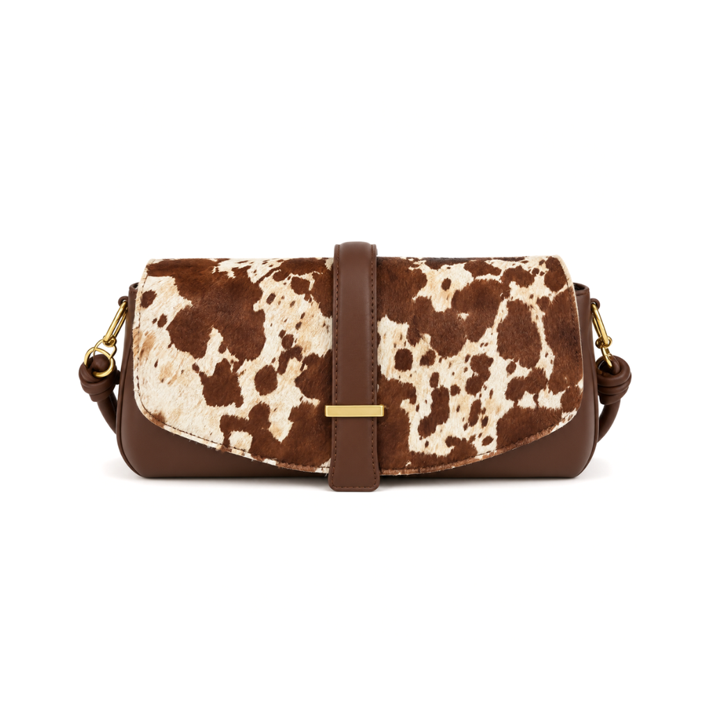 A brown and cream cow-print handbag with solid brown leather trim, a central strap closure, and gold-tone hardware, shown against a plain white background.