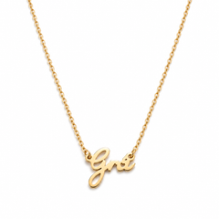 A delicate gold  plated chain necklace featuring a polished script pendant that spells Grá, displayed against a clean white background.
