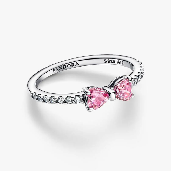 A Pandora ring featuring two pink heart-shaped gemstones on a silver band with small clear stones, shown on a clean white background.