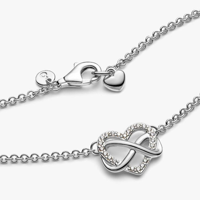 A silver chain bracelet featuring a heart-shaped infinity knot charm embellished with small clear stones, shown on a light gray background.