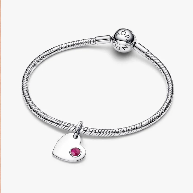 A silver snake chain bracelet with a heart-shaped charm featuring a small pink gemstone, displayed on a clean off-white background. The clasp is engraved with the brand name 'PANDORA'.