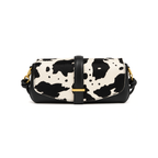 A small shoulder bag with a black and off-white cow print pattern on the front flap, solid black leather trim, a central black strap with a gold-tone buckle, and gold-tone side hardware, shown on a plain white background.